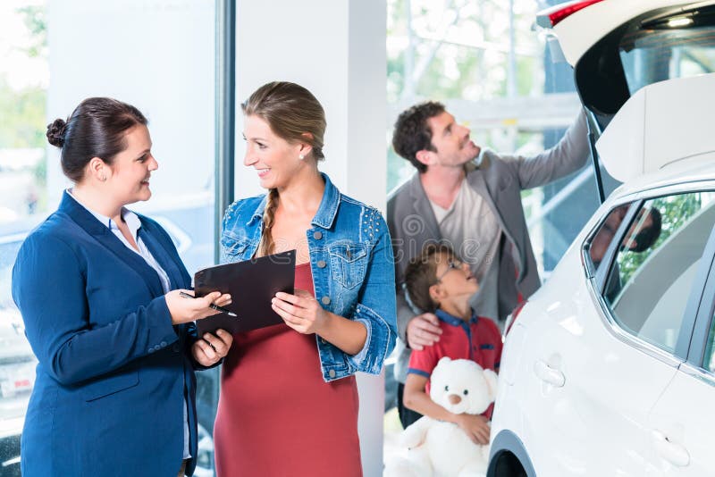 Family buying new car in auto dealer showroom, the sales lady shows the price list. Family buying new car in auto dealer showroom, the sales lady shows the price list