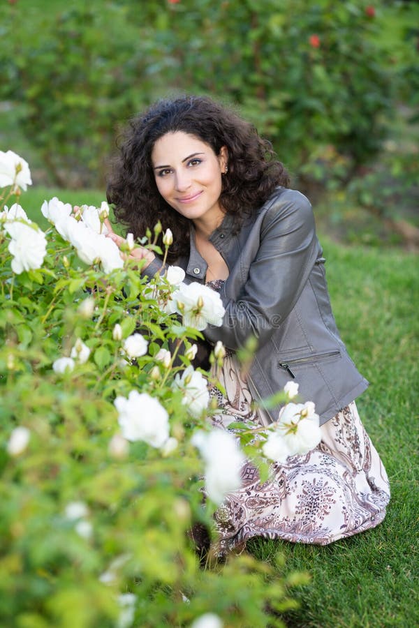 Kaukasische brunette junge Frau, die auf grünem Gras in einem Rosengarten nahe gelbem Rosenbusch, lächelnd mit den Zähnen sitzt u lizenzfreie stockbilder Kaukasische brunette junge Frau, die auf grünem Gras in einem Rosengarten nahe gelbem Rosenbusch, lächelnd mit den Zähnen sitzt u lizenzfreie stockbilder