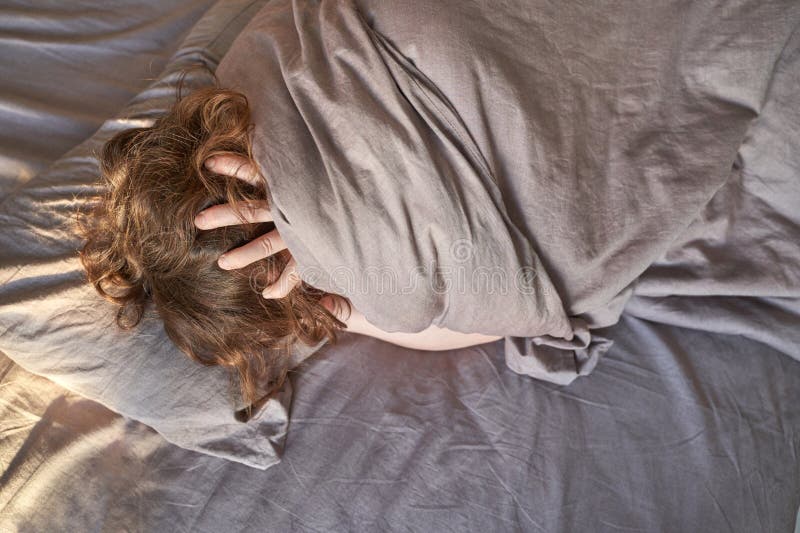 Kaukasische erwachsene Weibliche, in graue Decke verpackt und mit Händen am Kopf im Bett liegend lizenzfreie stockfotos