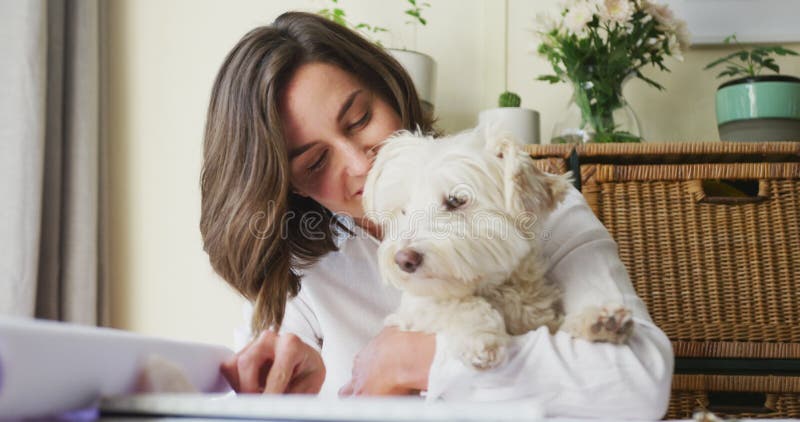 Kaukasische Frau, die von zu Hause aus arbeitet und ihren Hund kuschelt