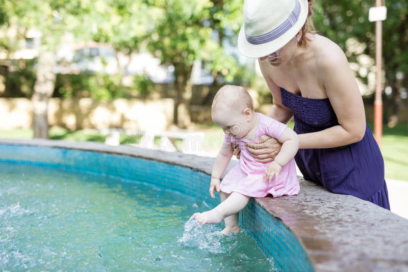 Kaukasische Holdingbabytochter der jungen Frau, während sie auf Seite des Brunnens und der baumelnden Beine sitzt stockbilder Kaukasische Holdingbabytochter der jungen Frau, während sie auf Seite des Brunnens und der baumelnden Beine sitzt stockbilder