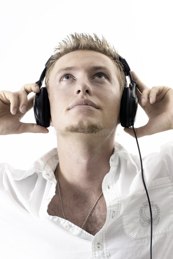 A caucasian man listening to headphones music with a white background. His head is facing upwards and both his hands are supporting the headset. Casual white clothes with a partially revealed chain around his neck. A caucasian man listening to headphones music with a white background. His head is facing upwards and both his hands are supporting the headset. Casual white clothes with a partially revealed chain around his neck.
