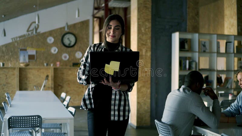 Kaukasische positieve vrouw die in openbare werkplaats met bakstenen muurbinnenland werken Mooi jong brunette in plaidoverhemd