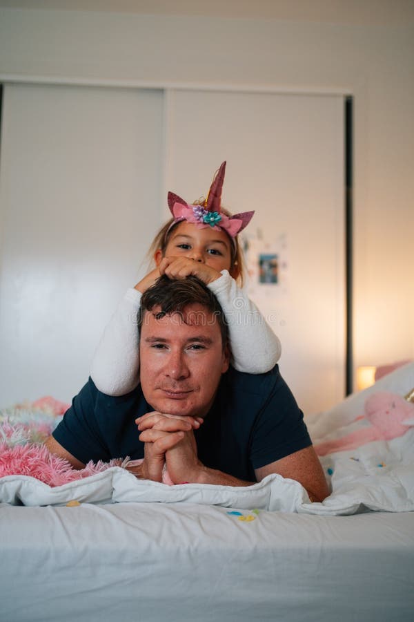Kaukasischer erwachsener Mann entspannt sich mit kaukasischem Kind mit unicorn Kopfband im Bett stockfotos