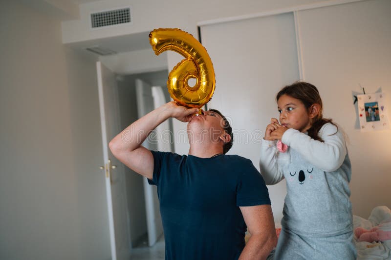 Kaukasischer erwachsener Mann mit junger hispanischer Mädchen, die Goldballon in einem gemütlichen Zimmer hält stockfoto