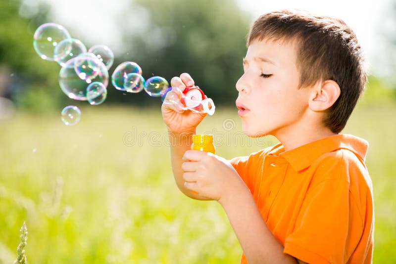 Kaukasischer Junge, der die Seifenblasen auf Natur durchbrennt lizenzfreies stockfoto Kaukasischer Junge, der die Seifenblasen auf Natur durchbrennt lizenzfreies stockfoto