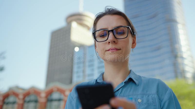 Kaukasisk kvinna i glasögon som går runt i staden och använder smartphone