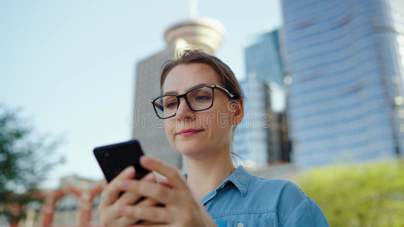 Kaukasisk kvinna i glasögon som går runt i staden och använder smartphone