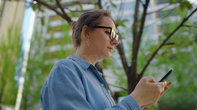 Kaukasisk kvinna i glasögon som går runt i staden och använder smartphone