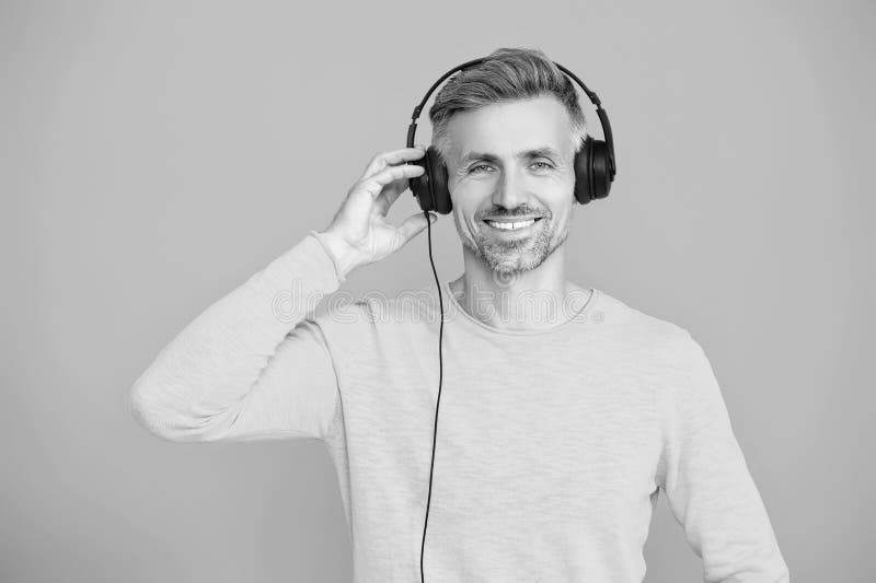 Kaukasisk man isolerad på blå. Mature man lyssnar på ljud. Mature man lyssnar på musik i hörlurar. Musikkoncept. Modern lycklig arkivfoton