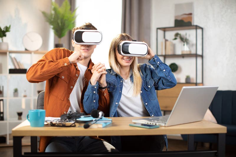 Kaukasiskt par i vr glasögon som sitter vid bordet med bärbar dator royaltyfria foton