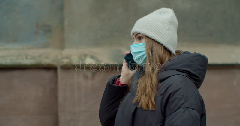 Kaukaska młoda stylowa kobieta w masce ochronnej rozmawiająca przez komórkę na ulicy. piękna szczęśliwa kobieta