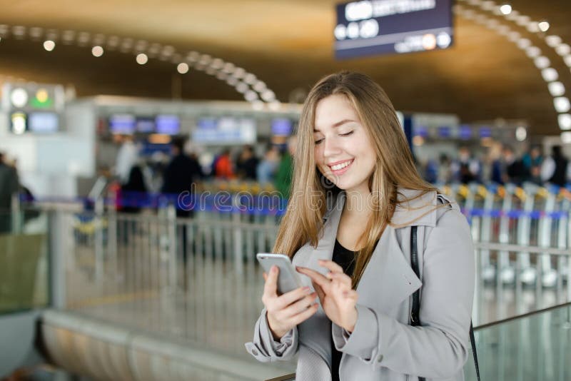 Kaukaska żeńskiej osoby pisać na maszynie wiadomość smartphone przy lotniskiem, jest ubranym żakiet obraz royalty free Kaukaska żeńskiej osoby pisać na maszynie wiadomość smartphone przy lotniskiem, jest ubranym żakiet obraz royalty free