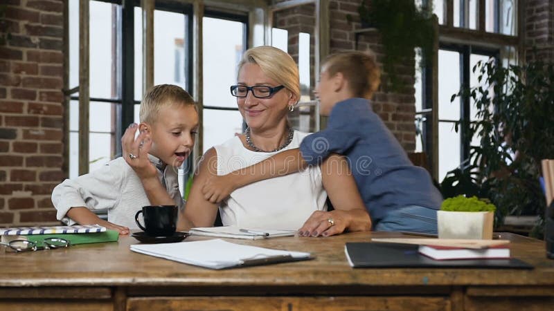 Kaukaski w średnim wieku kobieta pracuje z papierowymi dokumentami gdy jej śliczni wiek dojrzewania wnuki wchodzi jej biuro zbiory