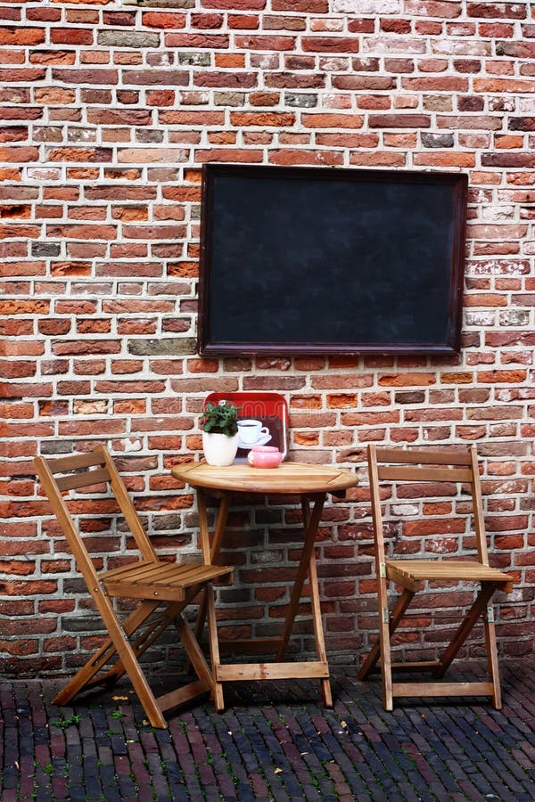 Small wooden table and chairs in front of a brick wall with a black board. Small wooden table and chairs in front of a brick wall with a black board.