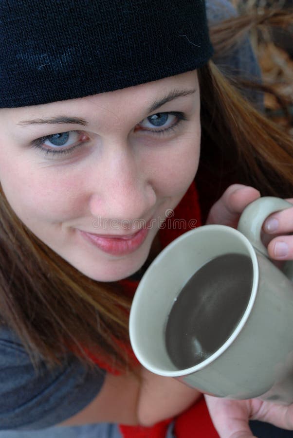 A young woman sits with her coffee cup and smiles. A young woman sits with her coffee cup and smiles