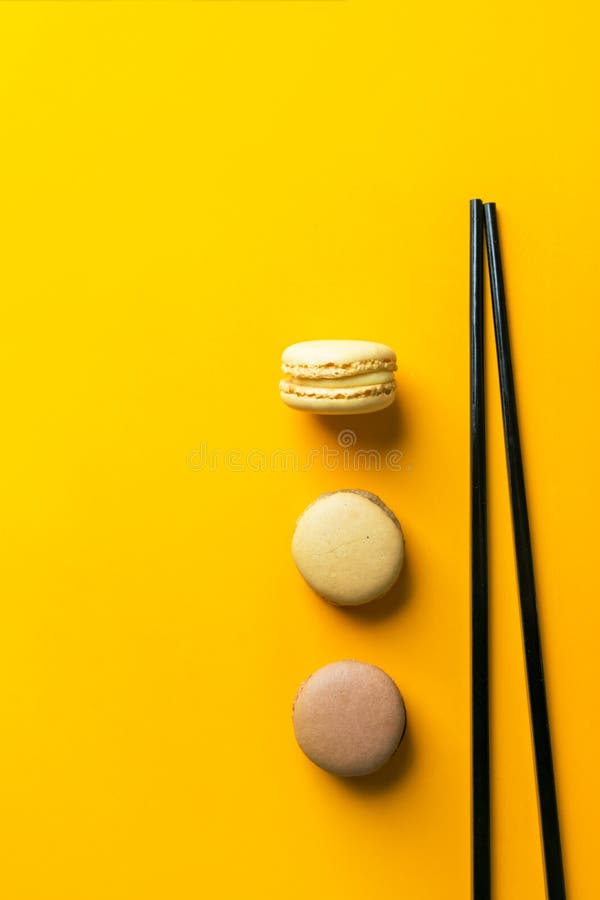Kawowi mokka karmelu macarons rozkładający w pionowo rzędzie na jaskrawym żółtym tle z czarnymi chopsticks Kreatywnie karmowy poj obraz royalty free Kawowi mokka karmelu macarons rozkładający w pionowo rzędzie na jaskrawym żółtym tle z czarnymi chopsticks Kreatywnie karmowy poj obraz royalty free