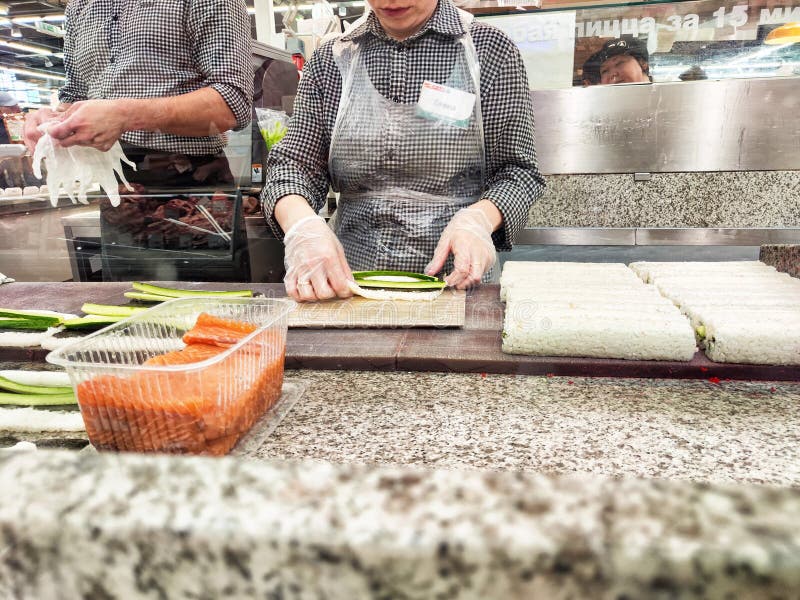 Kazan, Russia - April 26, 2024: Chefs prepare sushi rolls using fresh ingredients like cucumber and salmon in a bustling market environment during the day.