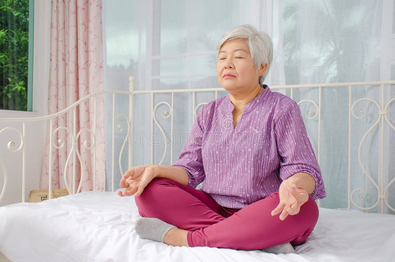 Keep calm and breath. Senior woman meditating in lotus position on bed at home, Healthy morning routine and meditation concept