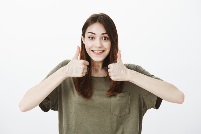 Keep up, you can do this. Pleased charming female friend in dark-green t-shirt, showing thumbs up and smiling happily stock photo Keep up, you can do this. Pleased charming female friend in dark-green t-shirt, showing thumbs up and smiling happily stock photo