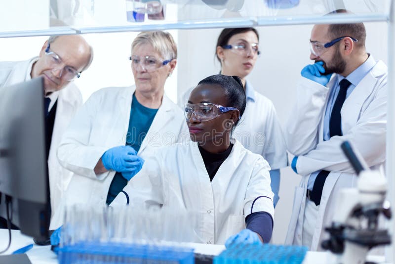 Chemists biologists conducting medical analysis using computer. African healthcare researcher in biochemistry laboratory wearing sterile equipment. Chemists biologists conducting medical analysis using computer. African healthcare researcher in biochemistry laboratory wearing sterile equipment.