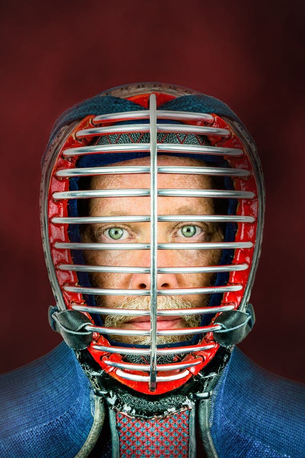Kendo - retrato ascendente cercano del kendoka con el casco Estudio tirado con el fondo rojo imagen de archivo libre de regalías Kendo - retrato ascendente cercano del kendoka con el casco Estudio tirado con el fondo rojo imagen de archivo libre de regalías
