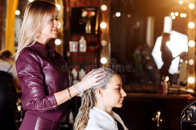 Keratin straightening, smoothing, hair colouring and treatment. Professional female beautician applying mask to female customer at royalty free stock image Keratin straightening, smoothing, hair colouring and treatment. Professional female beautician applying mask to female customer at royalty free stock image