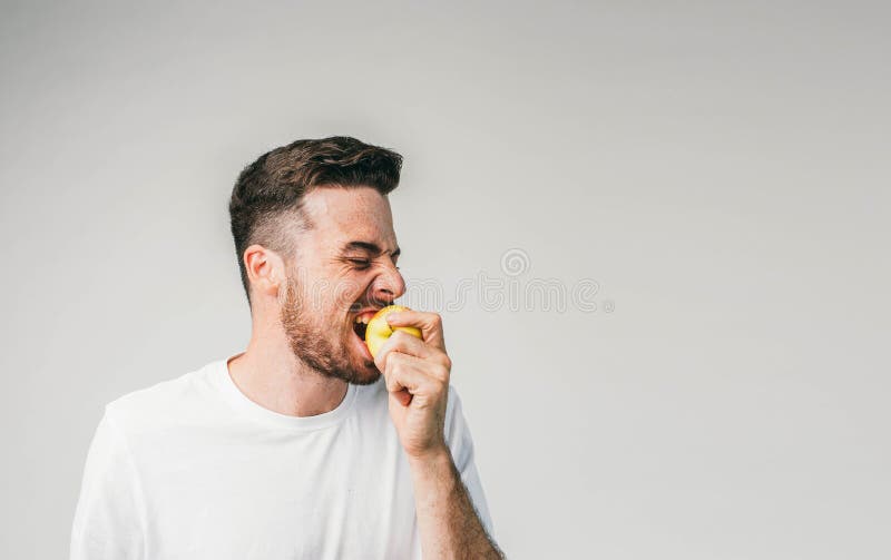 Kerl steht auf der linken Seite des Fotorahmens und beißt einen Apfel Diese Frucht ist so sauer, dass er nicht stoppen kann lizenzfreies stockbild Kerl steht auf der linken Seite des Fotorahmens und beißt einen Apfel Diese Frucht ist so sauer, dass er nicht stoppen kann lizenzfreies stockbild