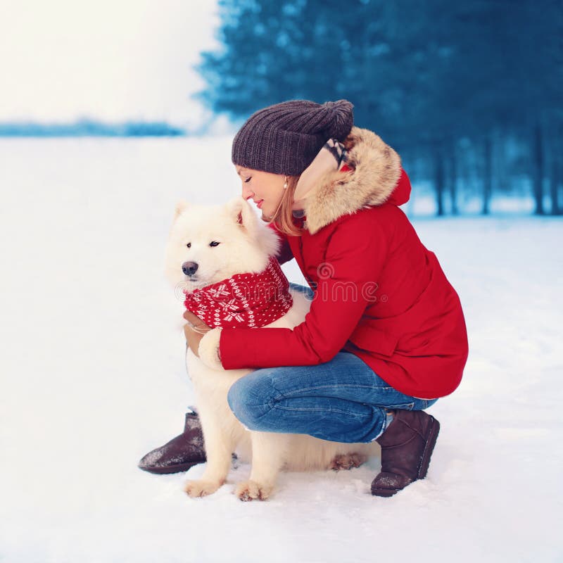 Christmas, winter and people concept - happy woman owner embracing white Samoyed dog outdoors. Christmas, winter and people concept - happy woman owner embracing white Samoyed dog outdoors