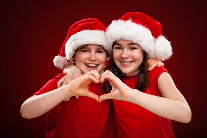 Kerstmistijd - meisje en jongen met Santa Claus Hats die hartteken tonen stock afbeelding Kerstmistijd - meisje en jongen met Santa Claus Hats die hartteken tonen stock afbeelding