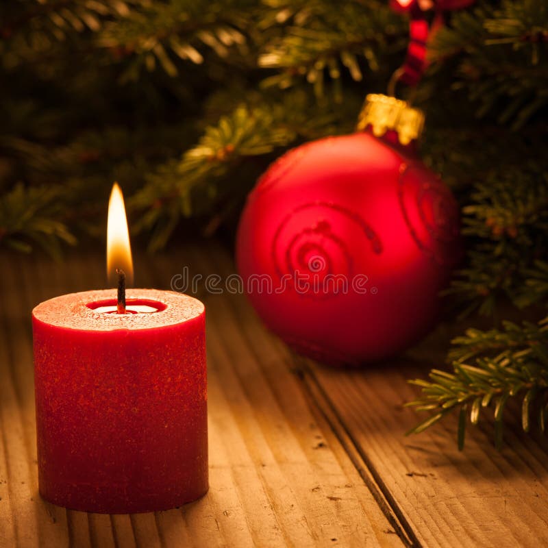 Candle light with red bauble on wooden desk with spruce branch in background. Candle light with red bauble on wooden desk with spruce branch in background