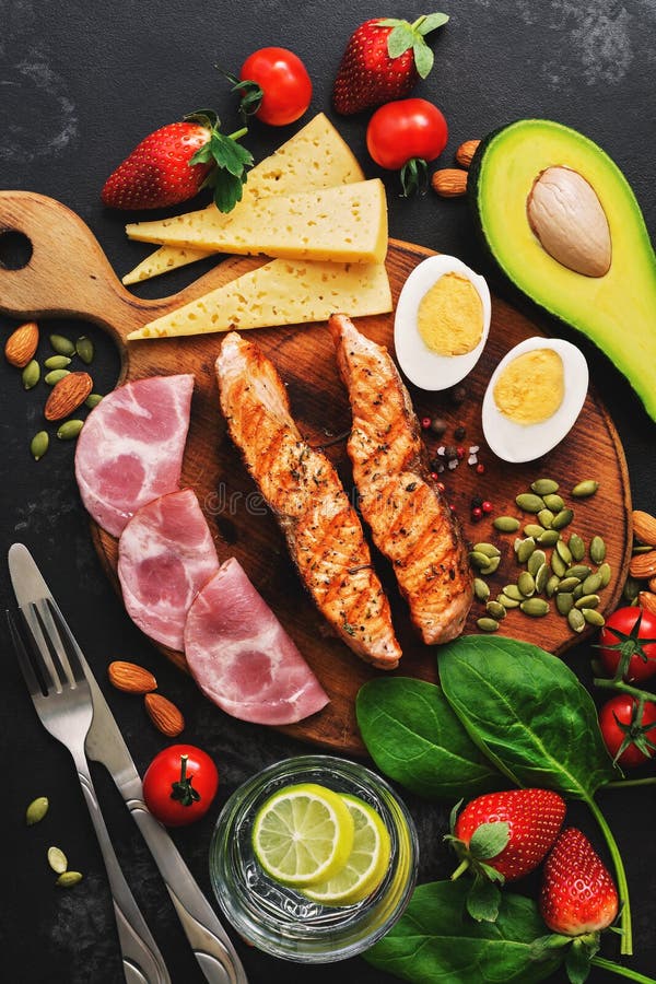 Keto, ketogenic диета, низкое содержание углевода Зажаренные семги, овощи, клубники, сыр, ветчина и вода с лимоном черный стоковая фотография Keto, ketogenic диета, низкое содержание углевода Зажаренные семги, овощи, клубники, сыр, ветчина и вода с лимоном черный стоковая фотография