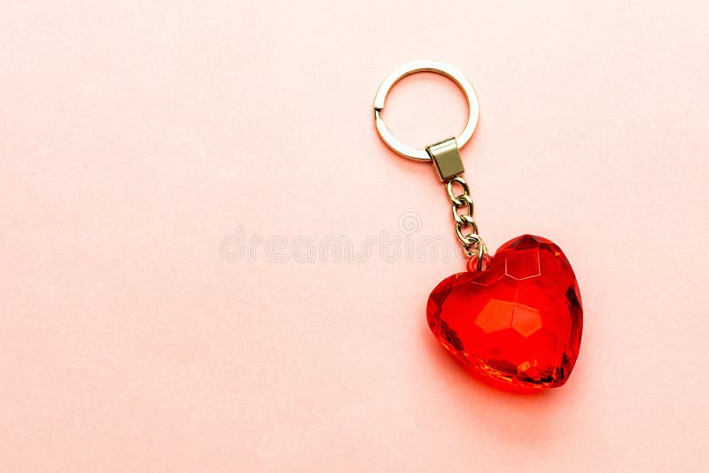 Keychain with red heart made of transparent cut glass or faceted stone on a soft pink paper background, copy space