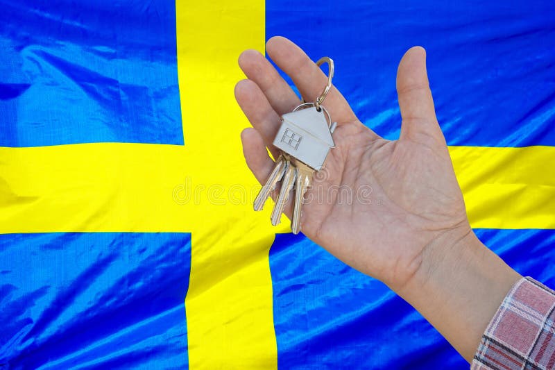 Keys to the apartment in a female hand on background of flag Sweden