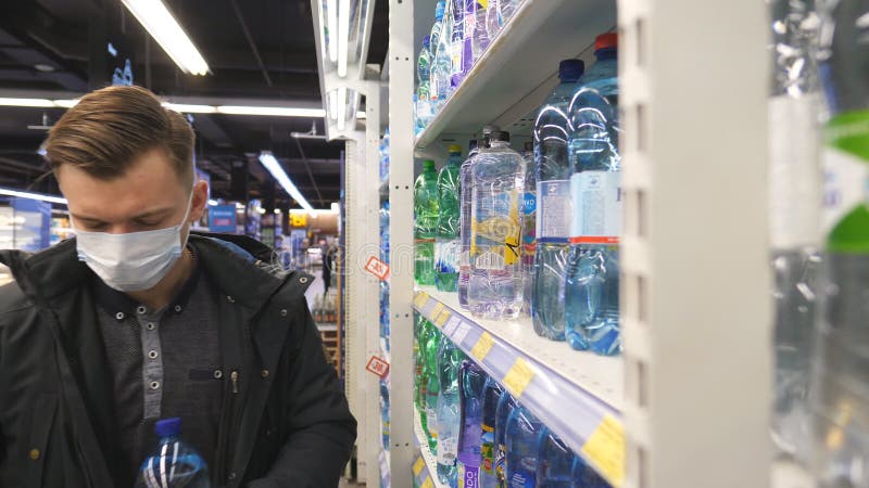 Kharkiv ucrania 18 de marzo de 2020 : joven con mascarilla médica eligiendo y comprando botellas de agua en el supermercado