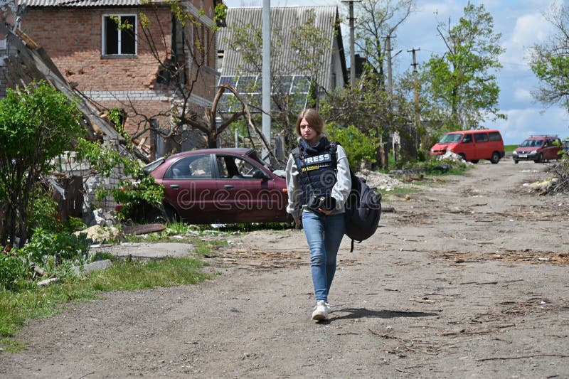 Kharkiv, Ukraine - May, 10, 2022: The girl-journalist is walking along the road among the broken houses. real war