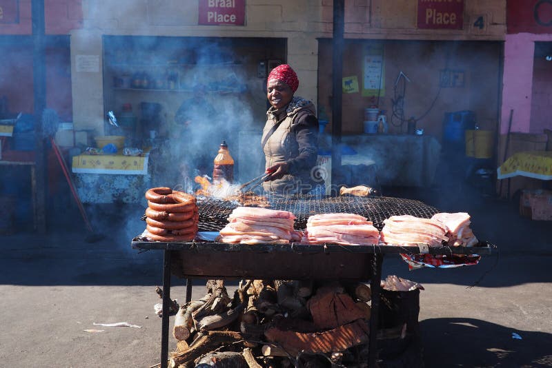 Khayelitsha, África do Sul - 29 de agosto de 2018: Mulher que cozinha o distrito do ina da carne em África do Sul imagem de stock royalty free Khayelitsha, África do Sul - 29 de agosto de 2018: Mulher que cozinha o distrito do ina da carne em África do Sul imagem de stock royalty free