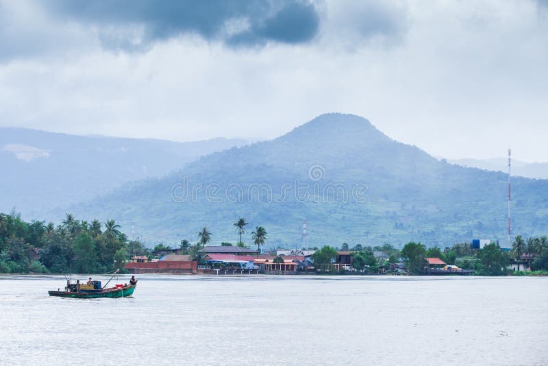 Khmer men and boy with old fishing boat going back home in the Praek Tuek Chhu River, cloudy over the Phnom Bokor mountain. Kampot