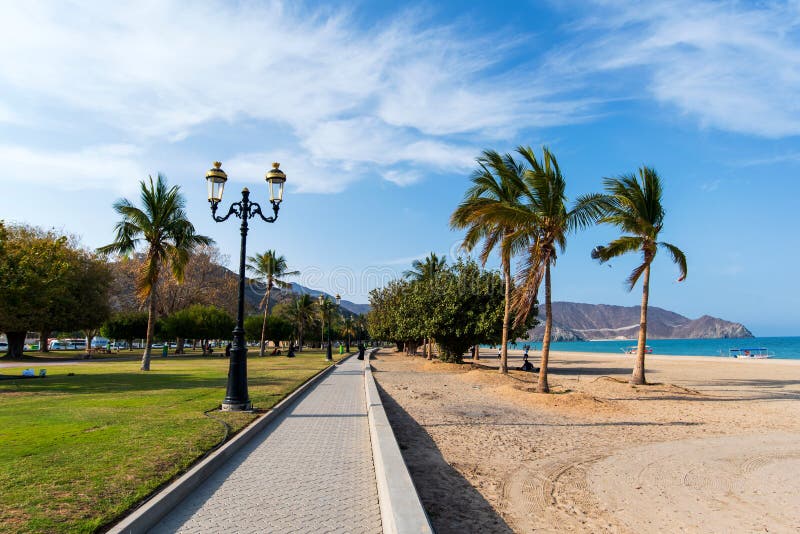 Khor Fakkan, United Arab Emirates - March 16, 2019: Khor Fakkan public beach in the emirate of Sharjah in United Arab Emirates on a sunny day uae sky gulf khorfakkan travel water sea peaceful vacation sand clouds palm tropical landscape mountain ocean scene view blue beautiful nature wave arabia park promenade outdoors fujairah coast arabic summer vibrant bay oman editorial. Khor Fakkan, United Arab Emirates - March 16, 2019: Khor Fakkan public beach in the emirate of Sharjah in United Arab Emirates on a sunny day uae sky gulf khorfakkan travel water sea peaceful vacation sand clouds palm tropical landscape mountain ocean scene view blue beautiful nature wave arabia park promenade outdoors fujairah coast arabic summer vibrant bay oman editorial