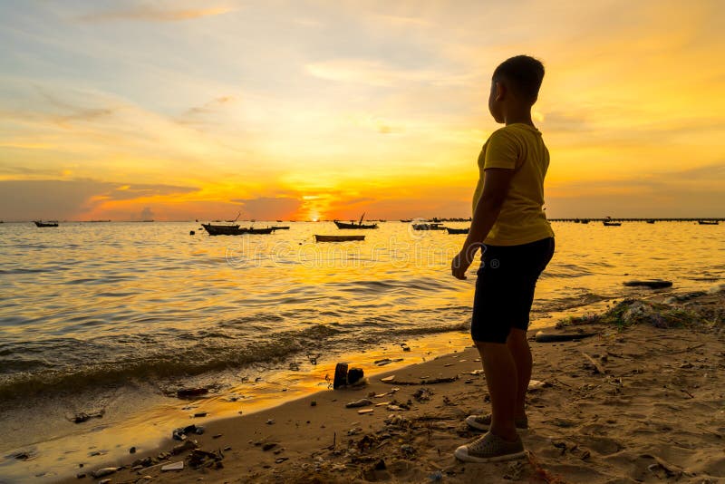 Kid boy looking the sea during sunset with fishing boat background