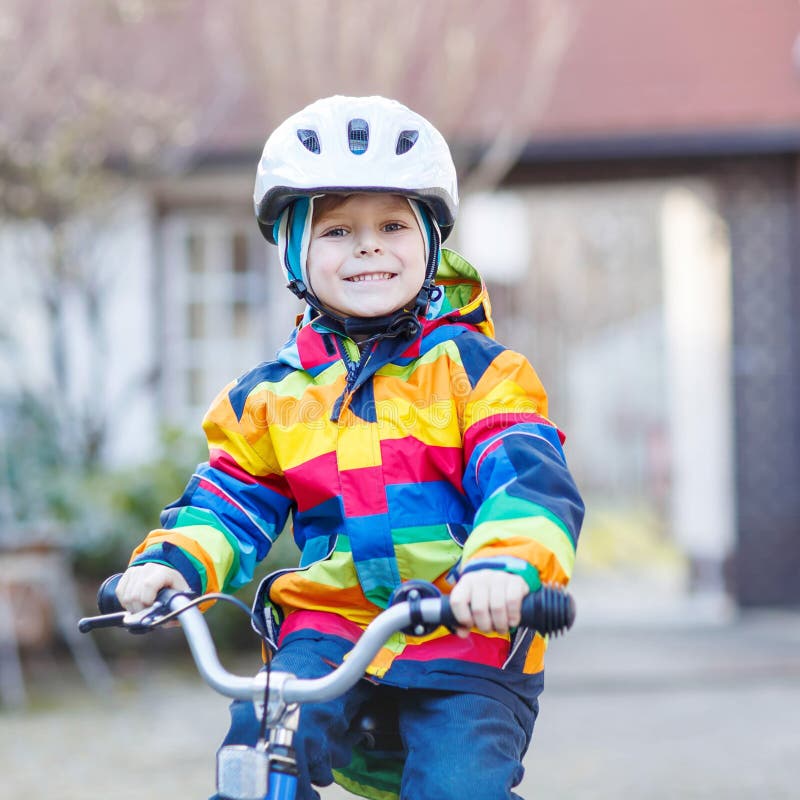 Kid boy in safety helmet and colorful raincoat riding bike, outd