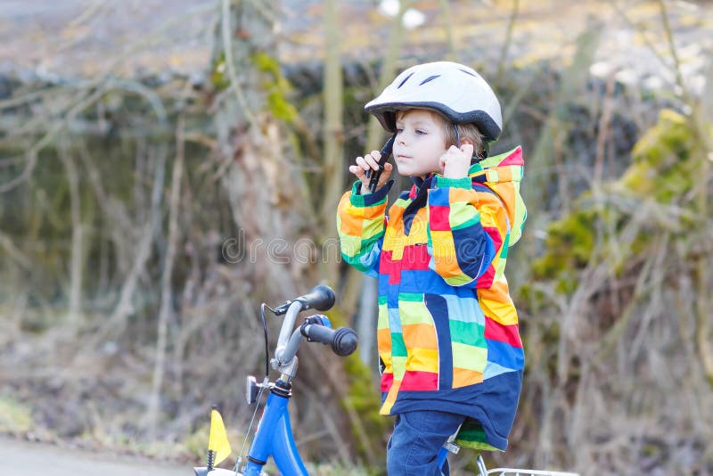 Kid boy in safety helmet and colorful raincoat riding bike, outd
