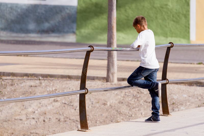 Kid boy standing alone on the bridge and looking down to the water