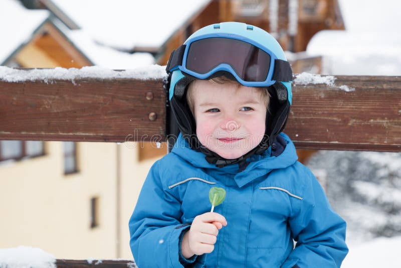 Kid boy wearing helmet, glasses and blue overalls at the ski resort