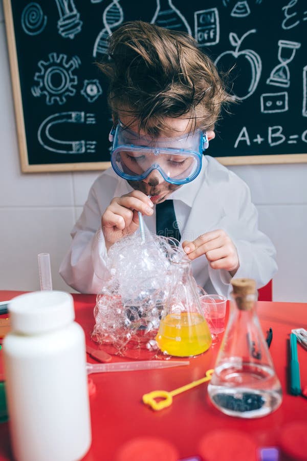 Crazy little boy scientist with glasses and dirty face doing soap bubbles with straw into glass. Crazy little boy scientist with glasses and dirty face doing soap bubbles with straw into glass