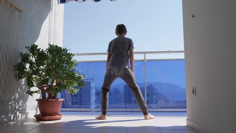 Kid doing sport exercises, running, jogging in place on the balcony. Sport, healhty lifestyle, active leisure. Stay home