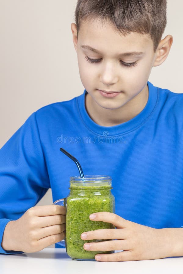 Kid drinking healthy green smoothie cocktail at home