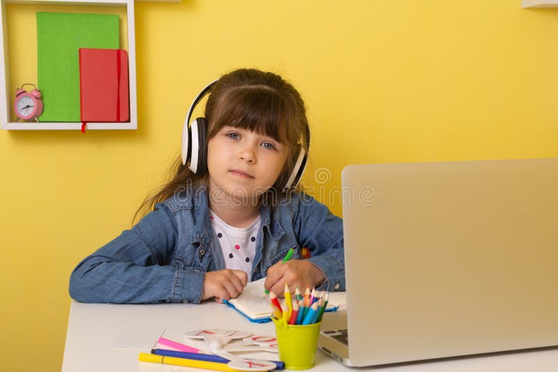 Kid girl with headphones using laptop at table in room. Online classes, teaching online. Child learning at home via virtual classes stock image