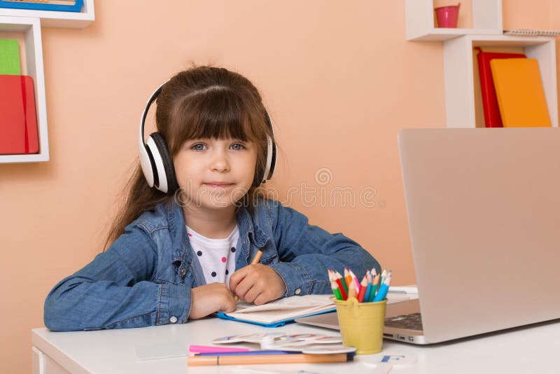 Kid girl with headphones using laptop at table in room. Online classes, teaching online. royalty free stock images Kid girl with headphones using laptop at table in room. Online classes, teaching online. royalty free stock images