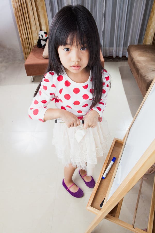 Kid girl writes on a white board with black mark pen.